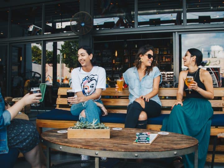 four women sitting on bench in storefront while drinking alcoholic beverages